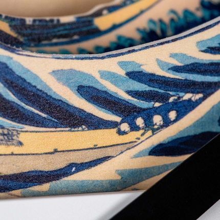 Close-up of a curved surface featuring an abstract pattern in blue, yellow, and beige tones with wavy lines and shapes. The design appears on a textured material, possibly fabric or synthetic.