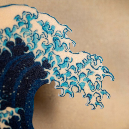 A close-up of a wave with white foam and blue water, inspired by traditional Japanese art, set against a plain beige background.