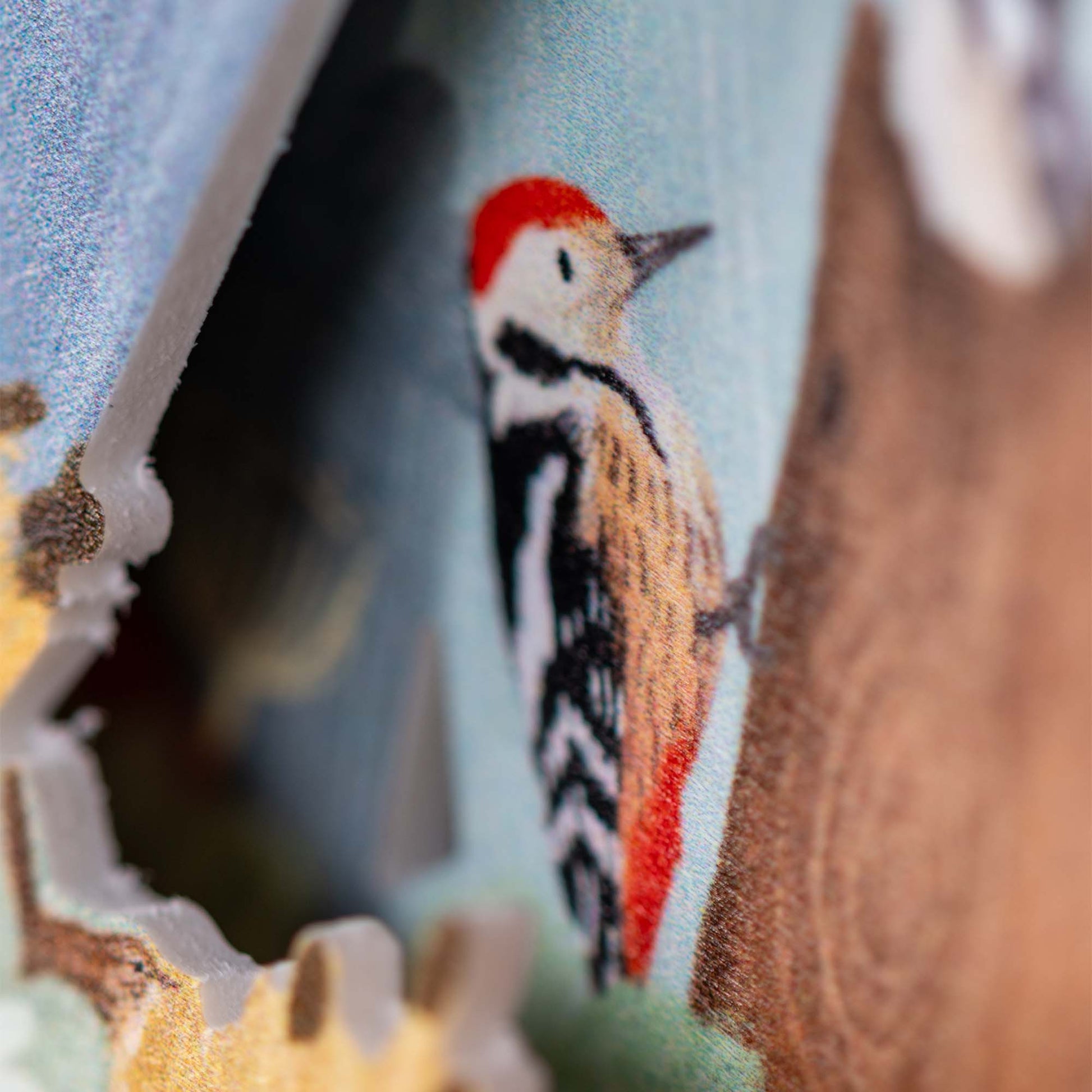 Close-up of an illustration of a woodpecker with a red head, black and white body, and yellowish wings, perched on a tree; the image appears on a textured or layered surface.
