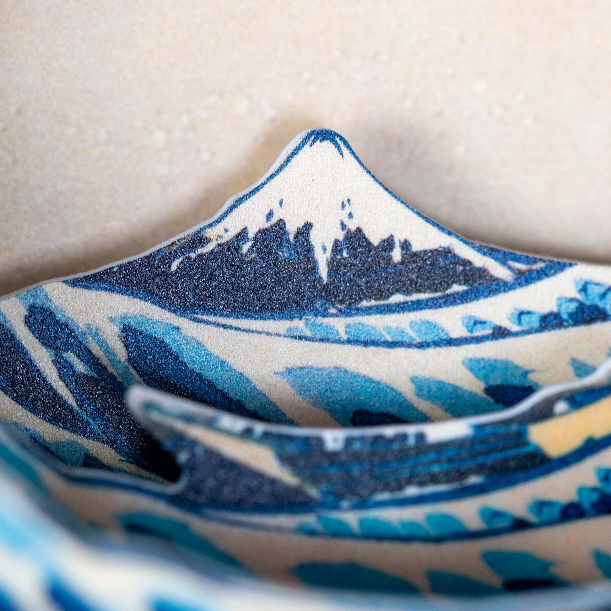 A close-up of the Hokusai Tide Art Clock highlights a blue and white mountain motif, inspired by the Great Wave Off Kanagawa. The rim mimics Mount Fuji’s peak, while textured patterns and varying blue hues enhance its unique design.