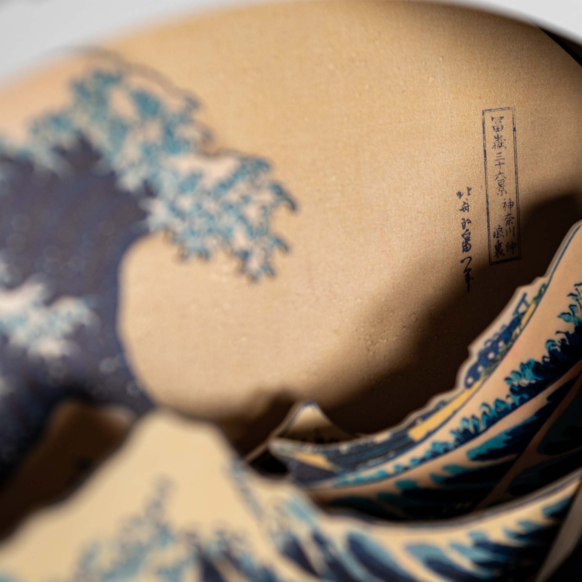Close-up of an artwork inspired by Hokusai’s The Great Wave off Kanagawa, showing a detailed blue wave and Japanese kanji text—ideal for fans of Hokusai's work.