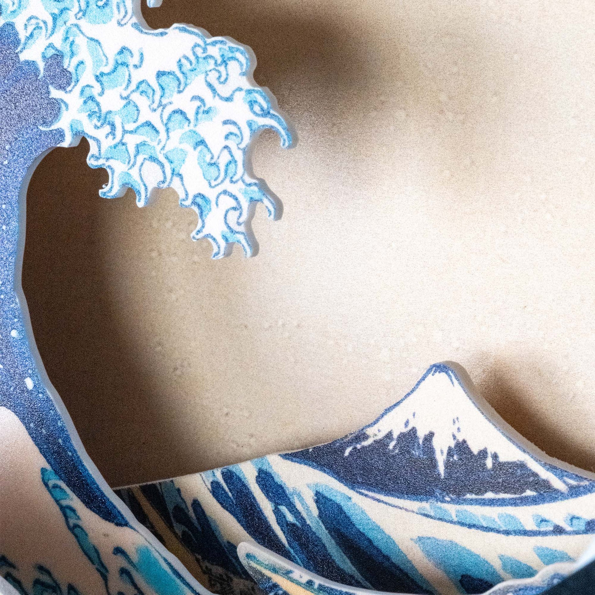 A close-up of the Hokusai Tide Art Clock shows blue and white waves with a snow-capped mountain, inspired by the Great Wave Off Kanagawa, set against a beige background.
