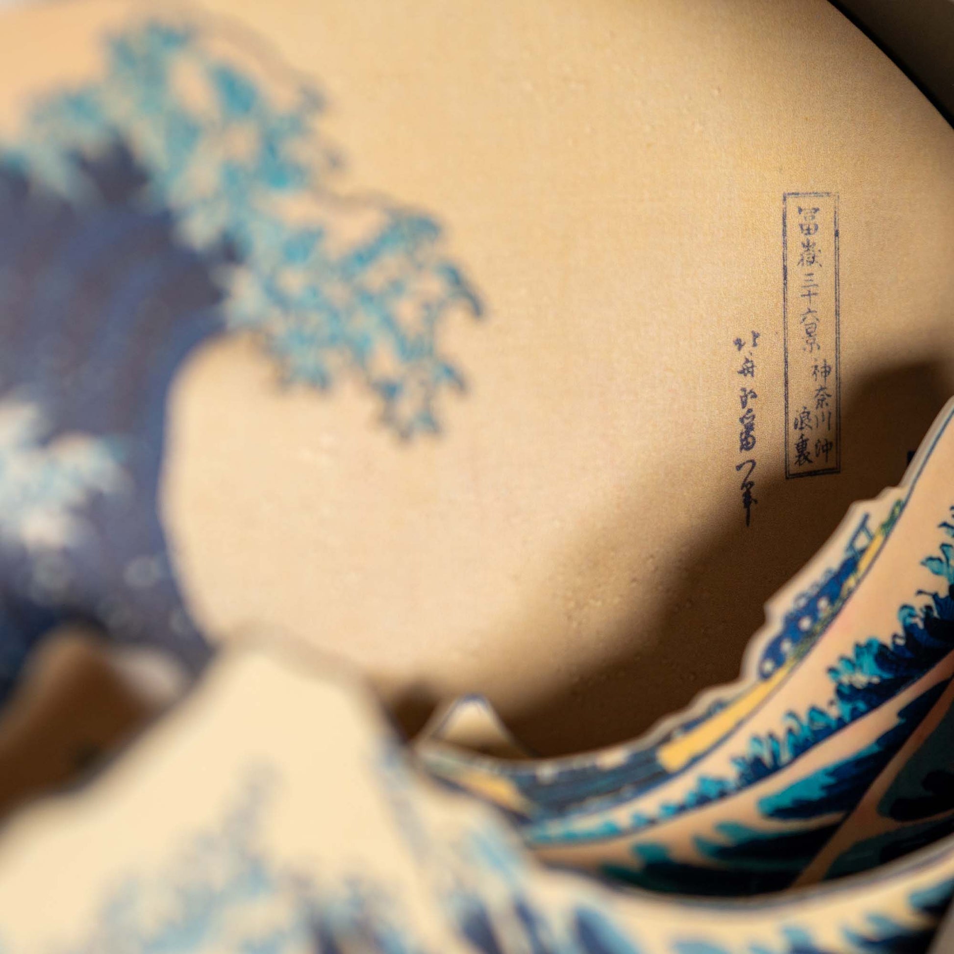 Close-up of the Hokusai Tide Art Clock, inspired by the Great Wave Off Kanagawa, featuring blue ocean waves, and Japanese calligraphy, intricate blue, cream, and tan details on a beige background.