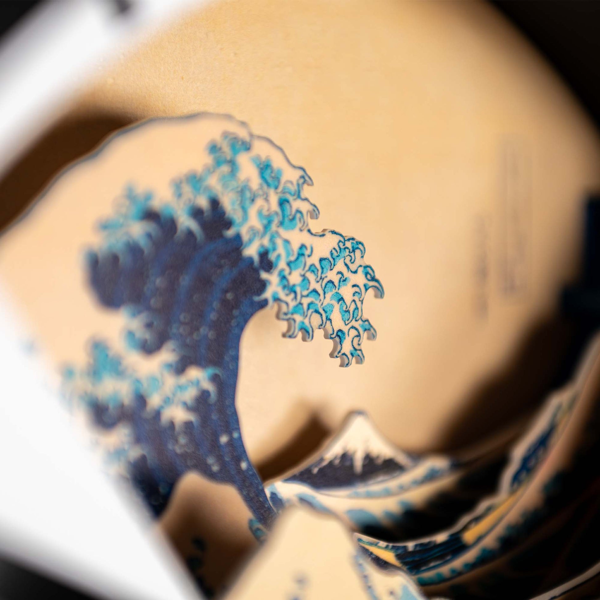 Close-up photo of a 3D paper model inspired by the Hokusai Tide Art Clock, showing stylized blue waves, echoing the iconic Great Wave Off Kanagawa design.