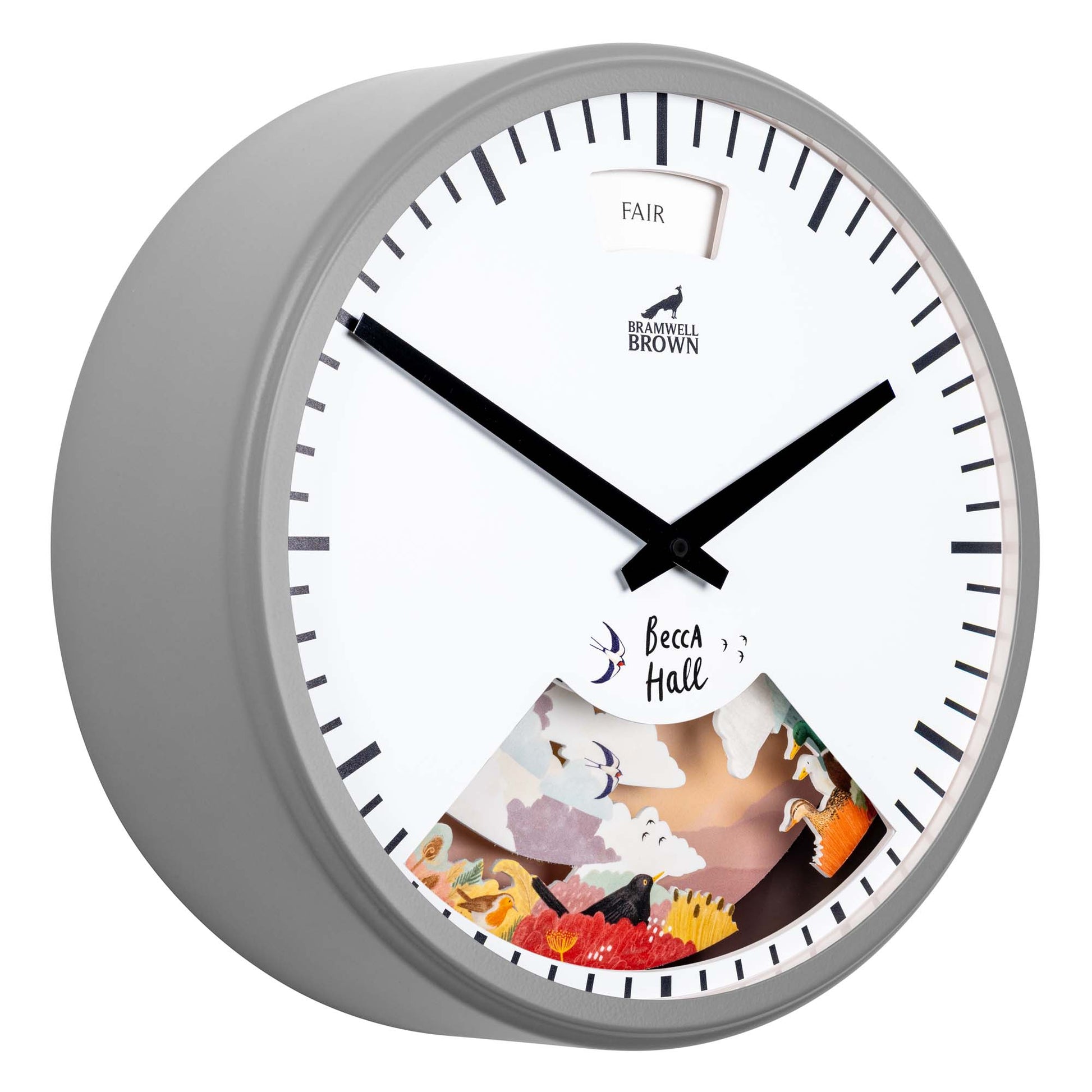 A round wall clock with a gray frame, black hands, and a white face. The lower part displays colorful paper illustrations and the word Becca Hall. A small window at the top shows the word FAIR.