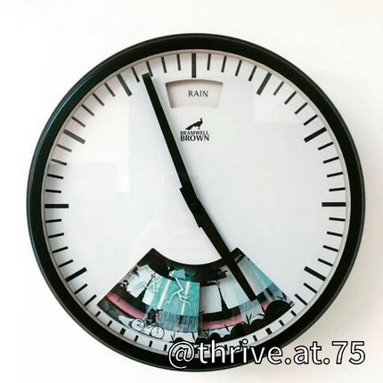A wall clock with a clear face shows RAIN at the top and the time at 4:00. Below the hands, colorful weather-related images are visible. The clock is branded BRAMWELL BROWN. Text @thrive.at.75 appears in the corner.