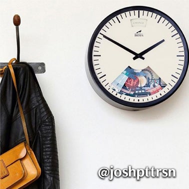 A clock with a section cut out, revealing colorful objects inside. The clock hangs on a white wall near a hook holding a black jacket and a brown handbag. @joshpttrsn is written on the image.