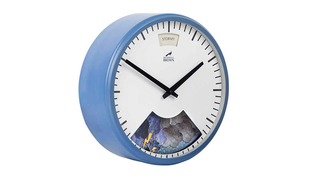 A round wall clock with a light blue frame, black hands, and minimal hour markers. The bottom section displays an image of clouds and lightning, and a small window at the top shows the word STORMY.