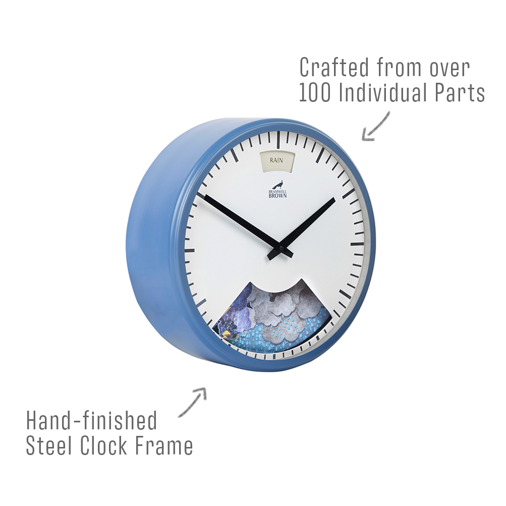 A round wall clock with a blue, hand-finished steel frame and black hands. Text points out the frame and notes the clock is crafted from over 100 individual parts. The clock face shows rain graphics at the bottom.